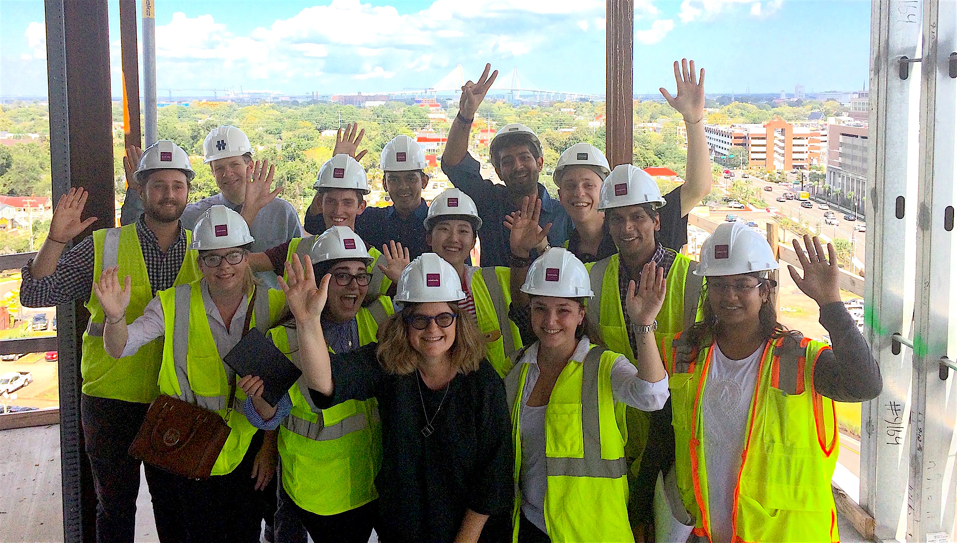 Group of students in construction vests and hard hats wave to camera