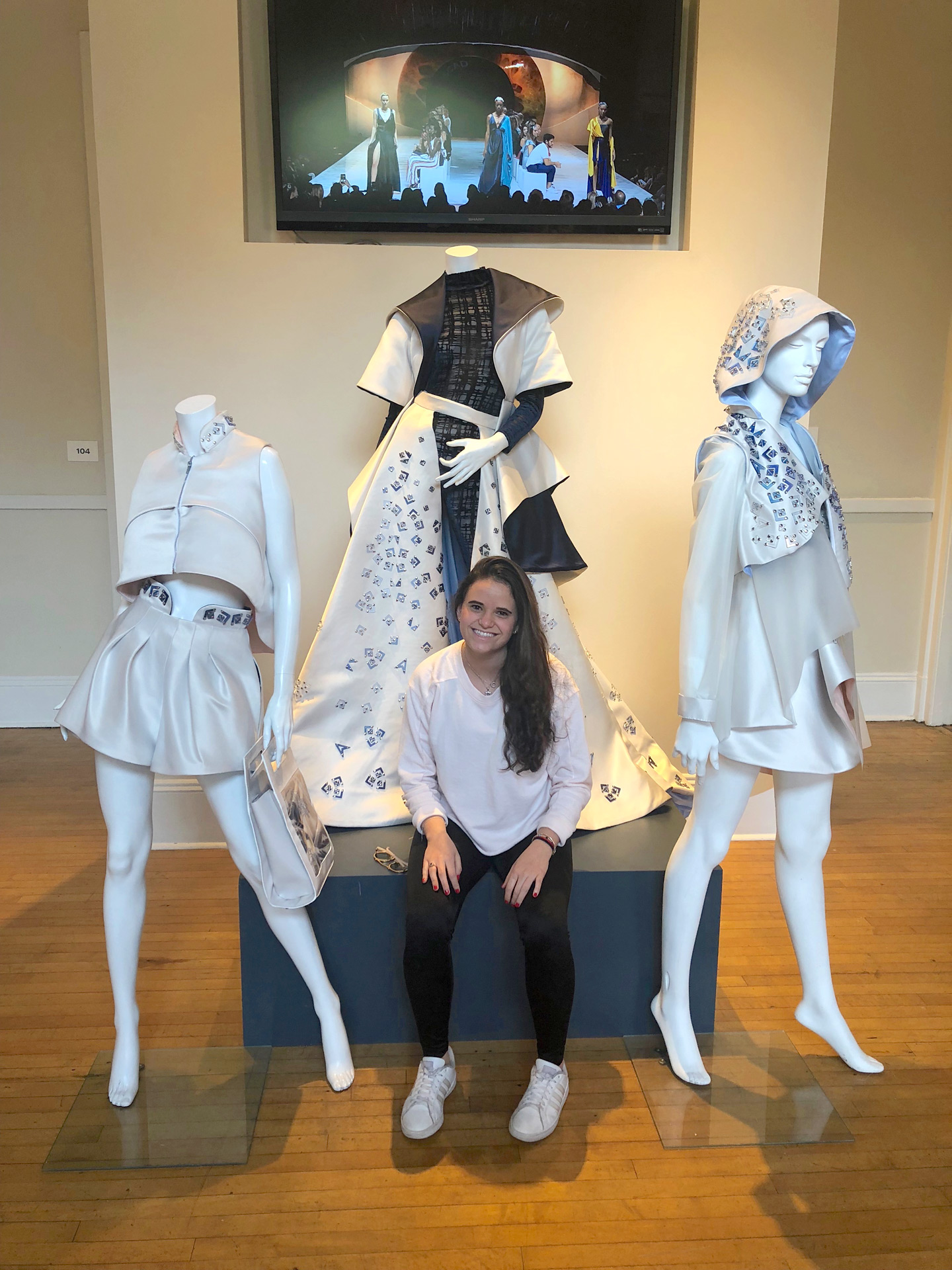 Rubinstein in front of three of her garments on mannequins 