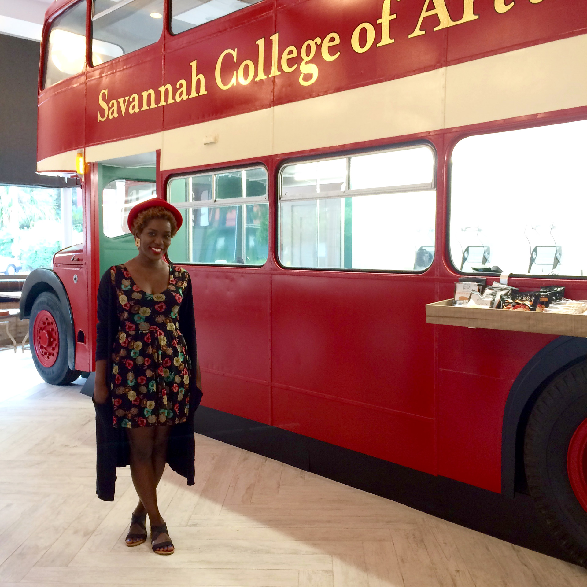 Alumna Merline Labissiere in front of red double decker bus at Art's Cafe