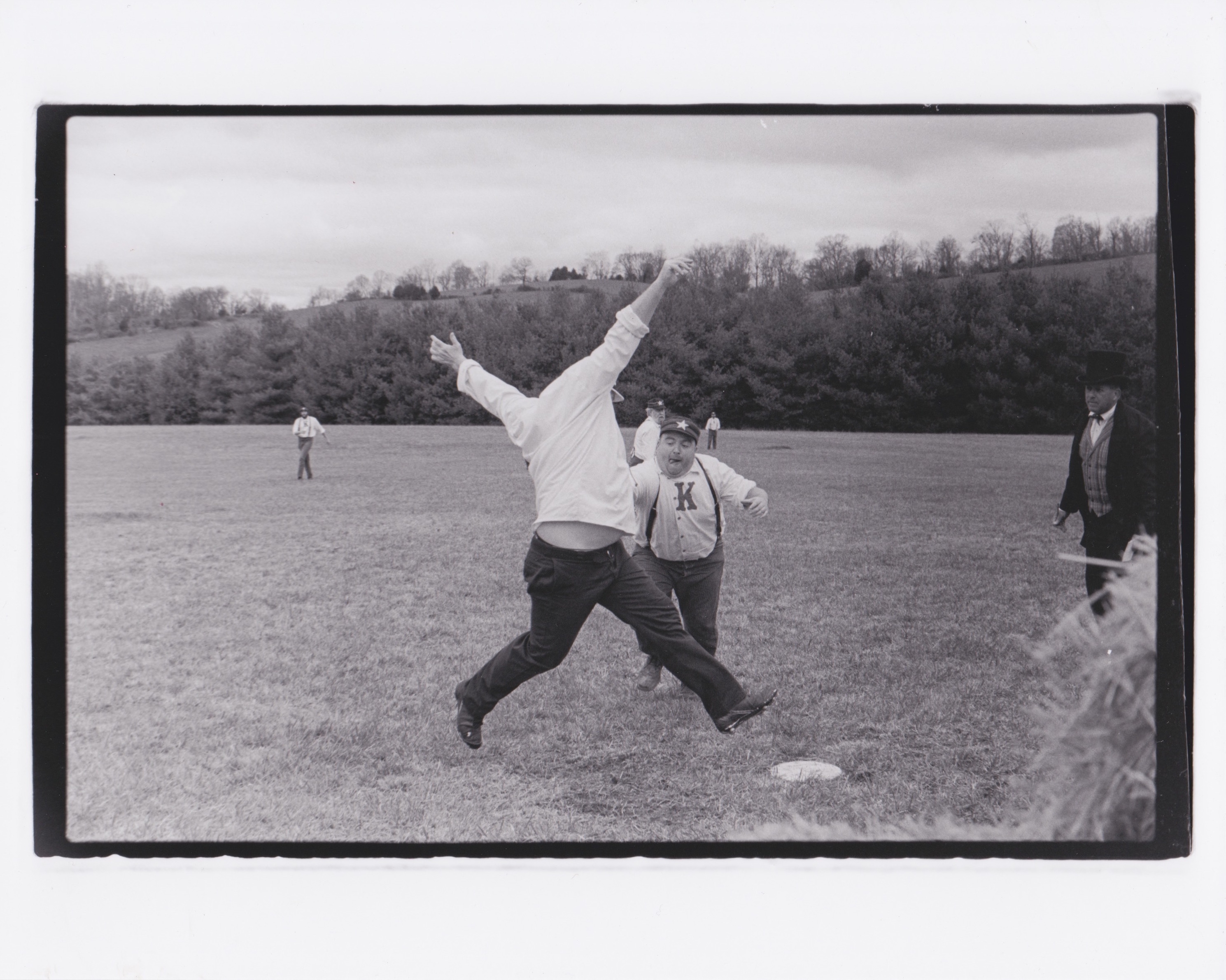 Black and white image of man running to baseball base as player stretches to tag him out