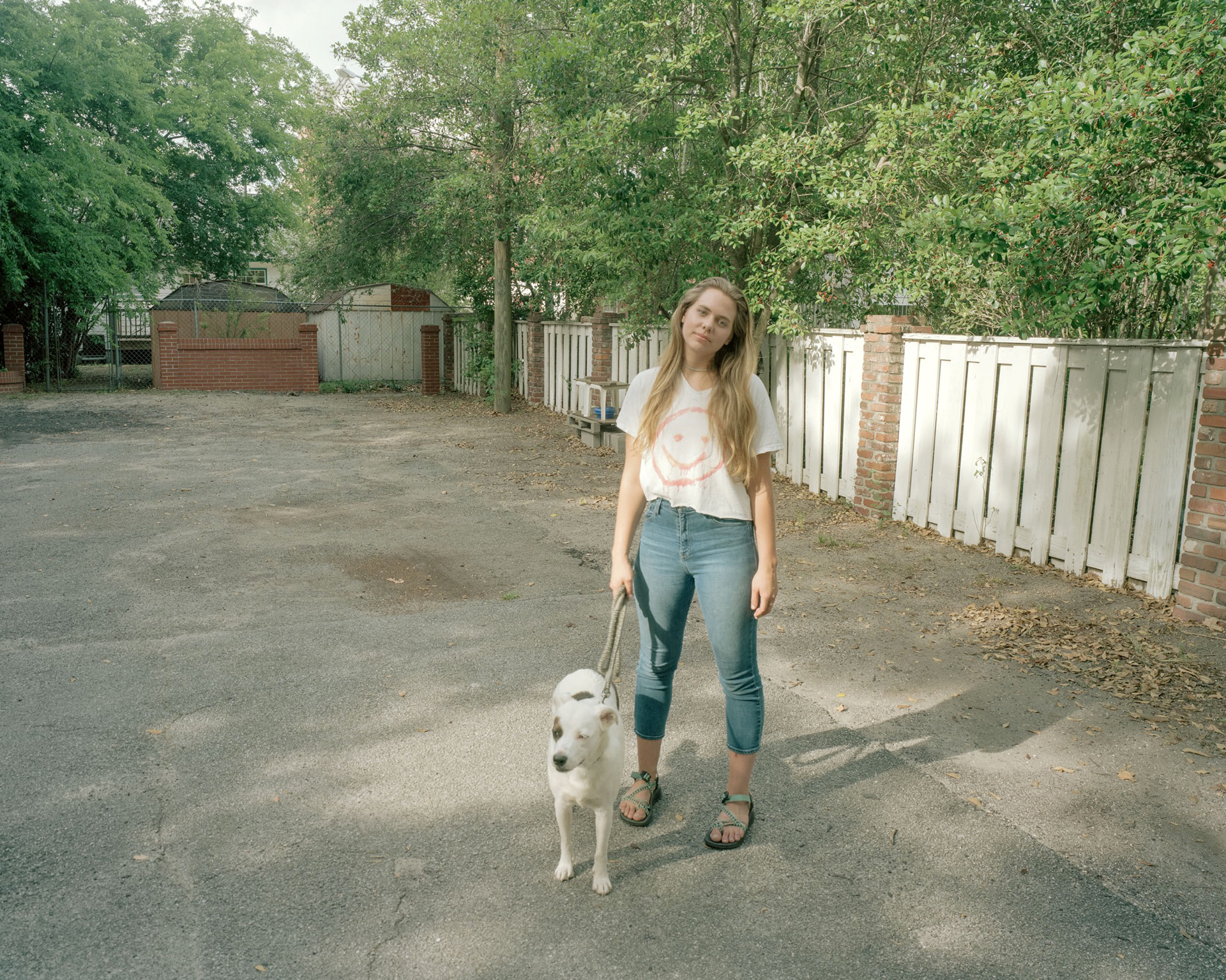 Young woman in sandals holds a leash with white dog and brown spots