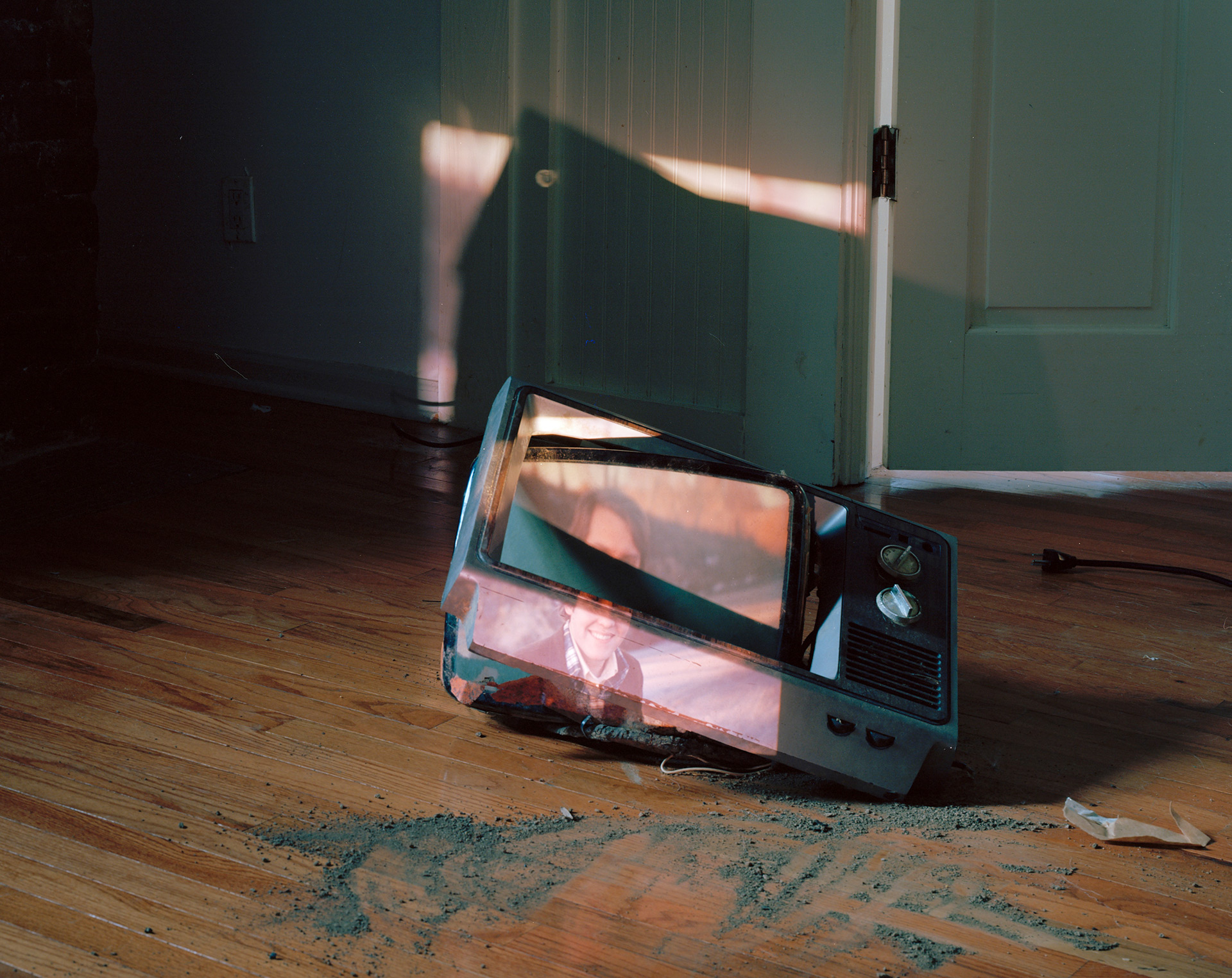 Broken television on wood floor with image of young man projected over it