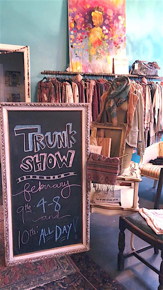 Chalkboard advertises a trunk show in front of racks of clothing