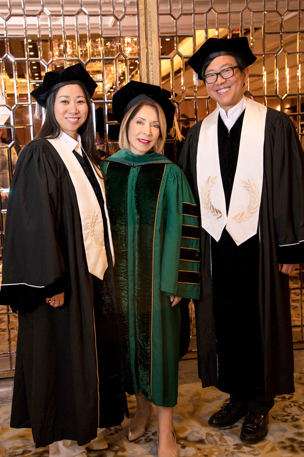 University president stands in green graduation gown and cap with two others