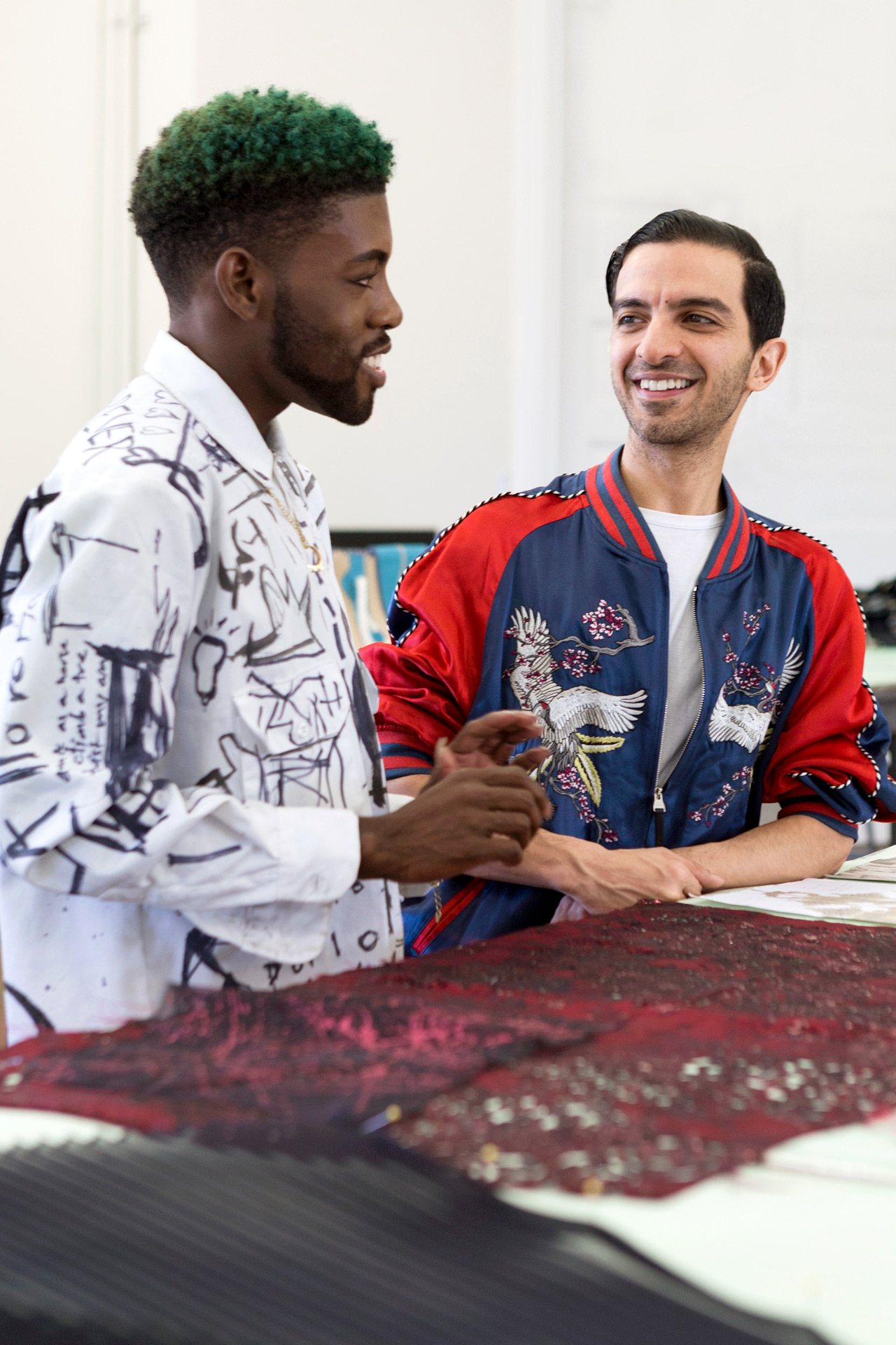 Two students discuss and smile over a worktop with red fabric on top