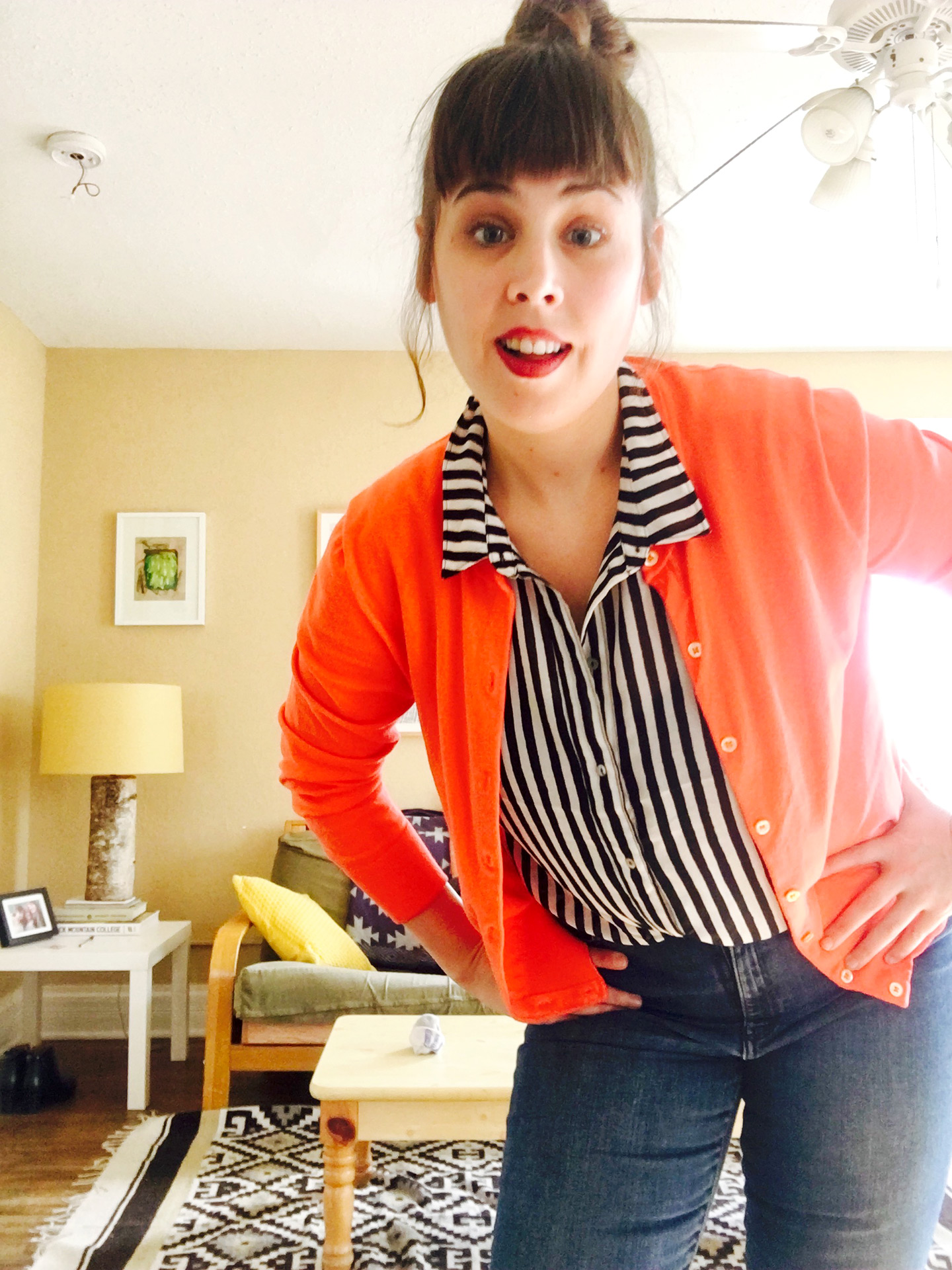 SCAD student and artist poses with her hands on her hips in orange sweater and black and white striped button down 