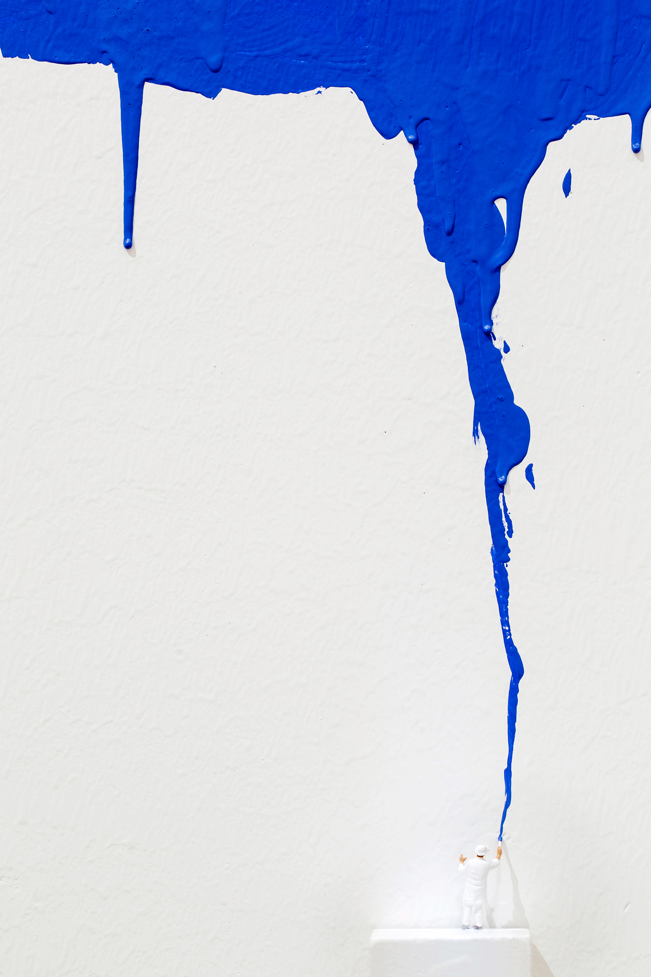 Tiny figurine paints oversized white background with blue paint