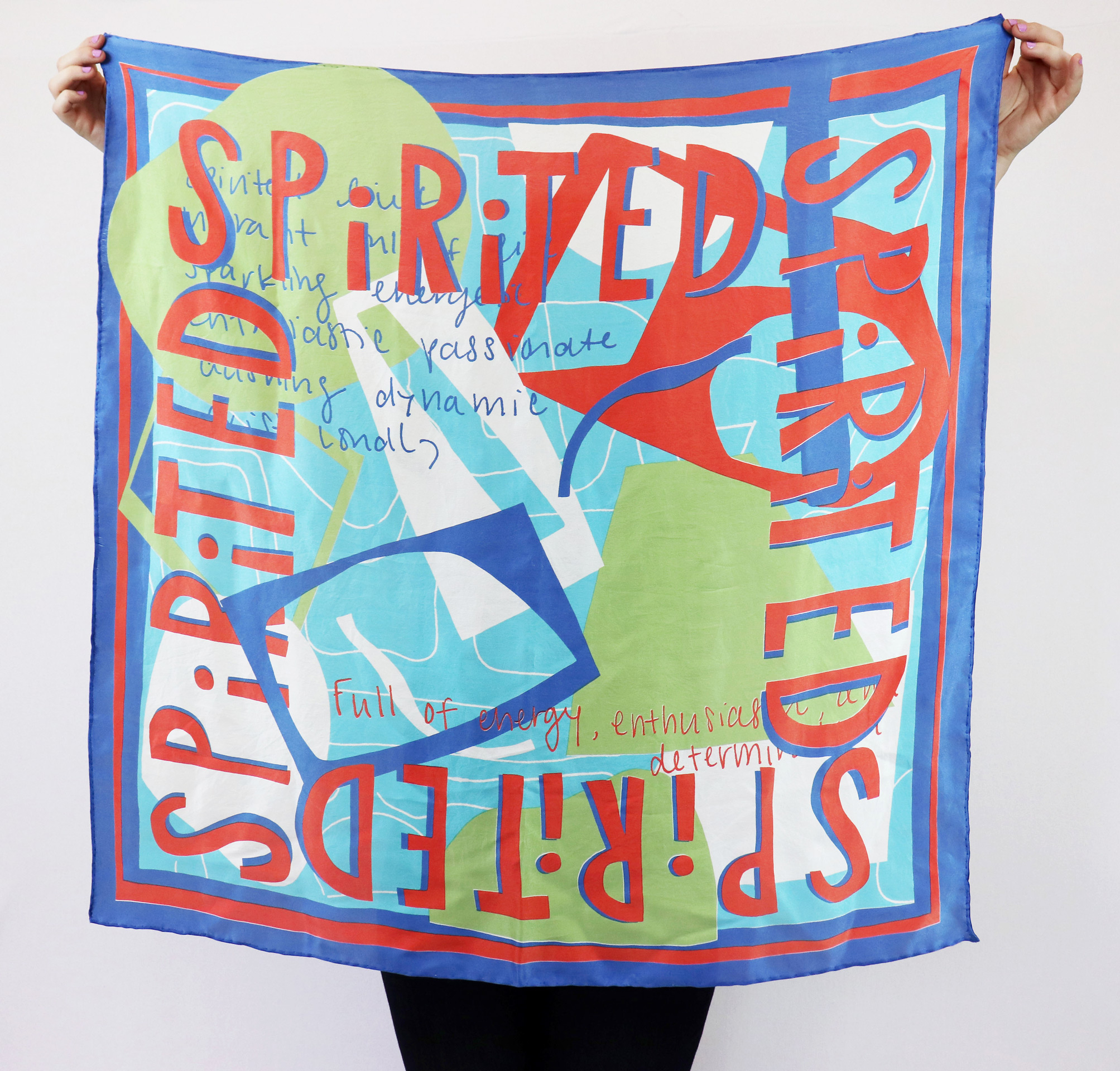 Anna Brettschneider holds up a square fabric printed with abstract shapes and the word spirited 