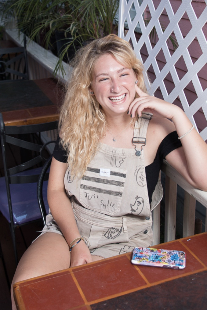 Hannah Amidon casually sits at a table and flashes a big smile 