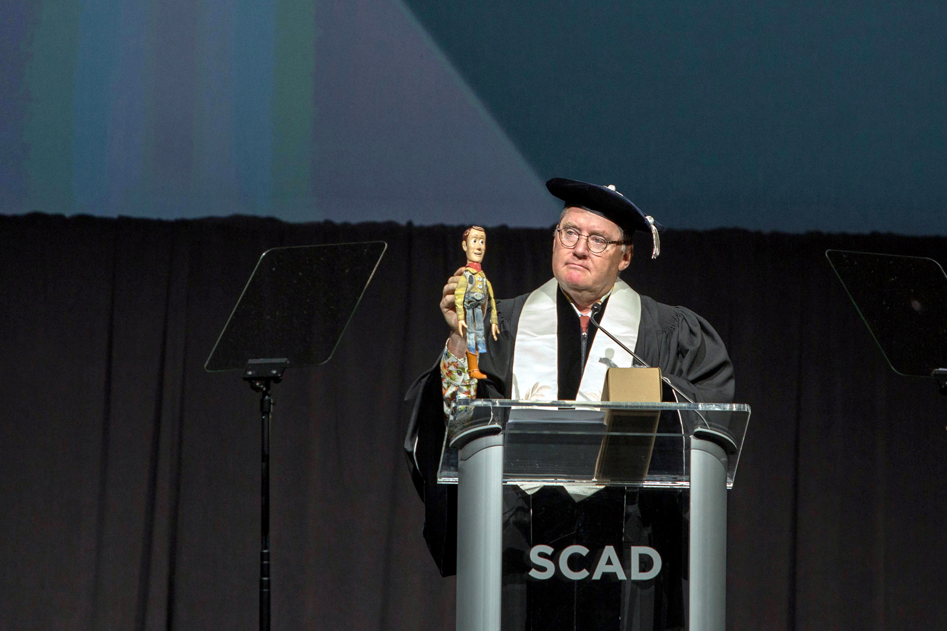 Commencement speaker John Lasseter holds a cartoon Woody doll