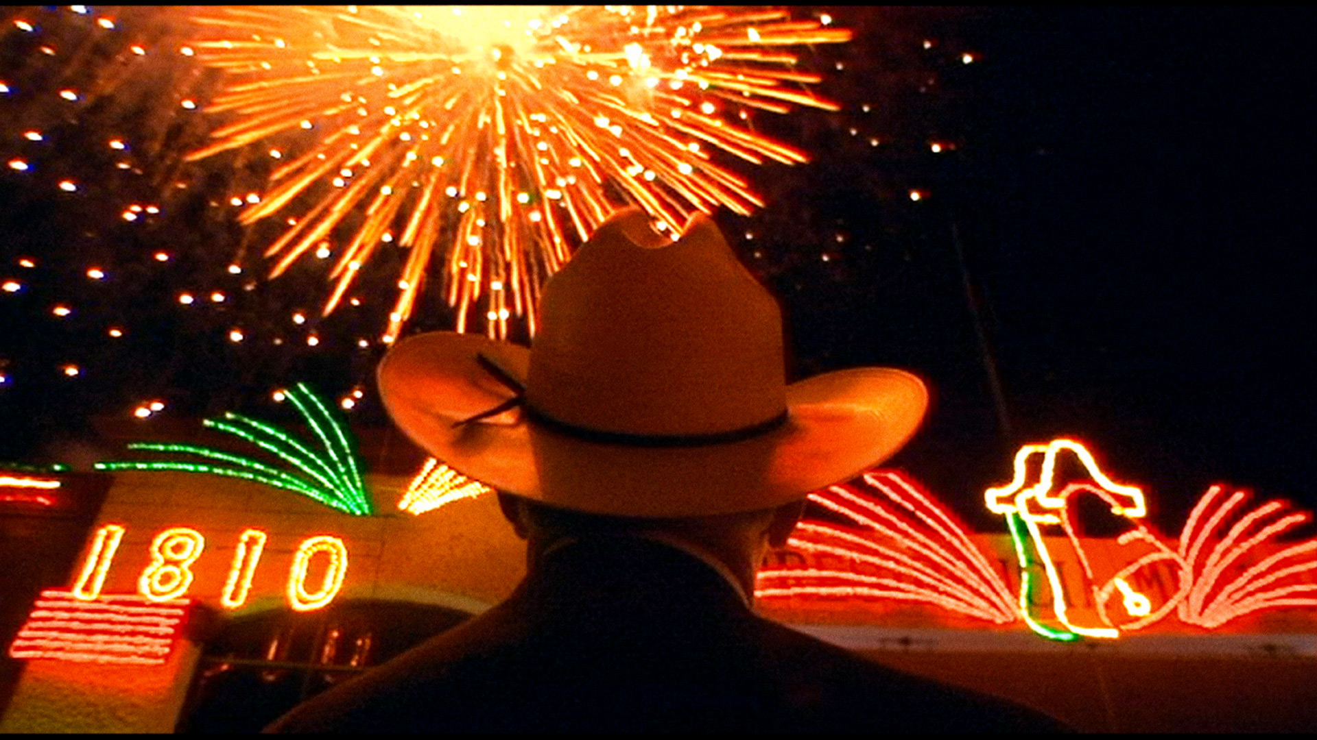 Back of man in cowboy hat looks at fireworks