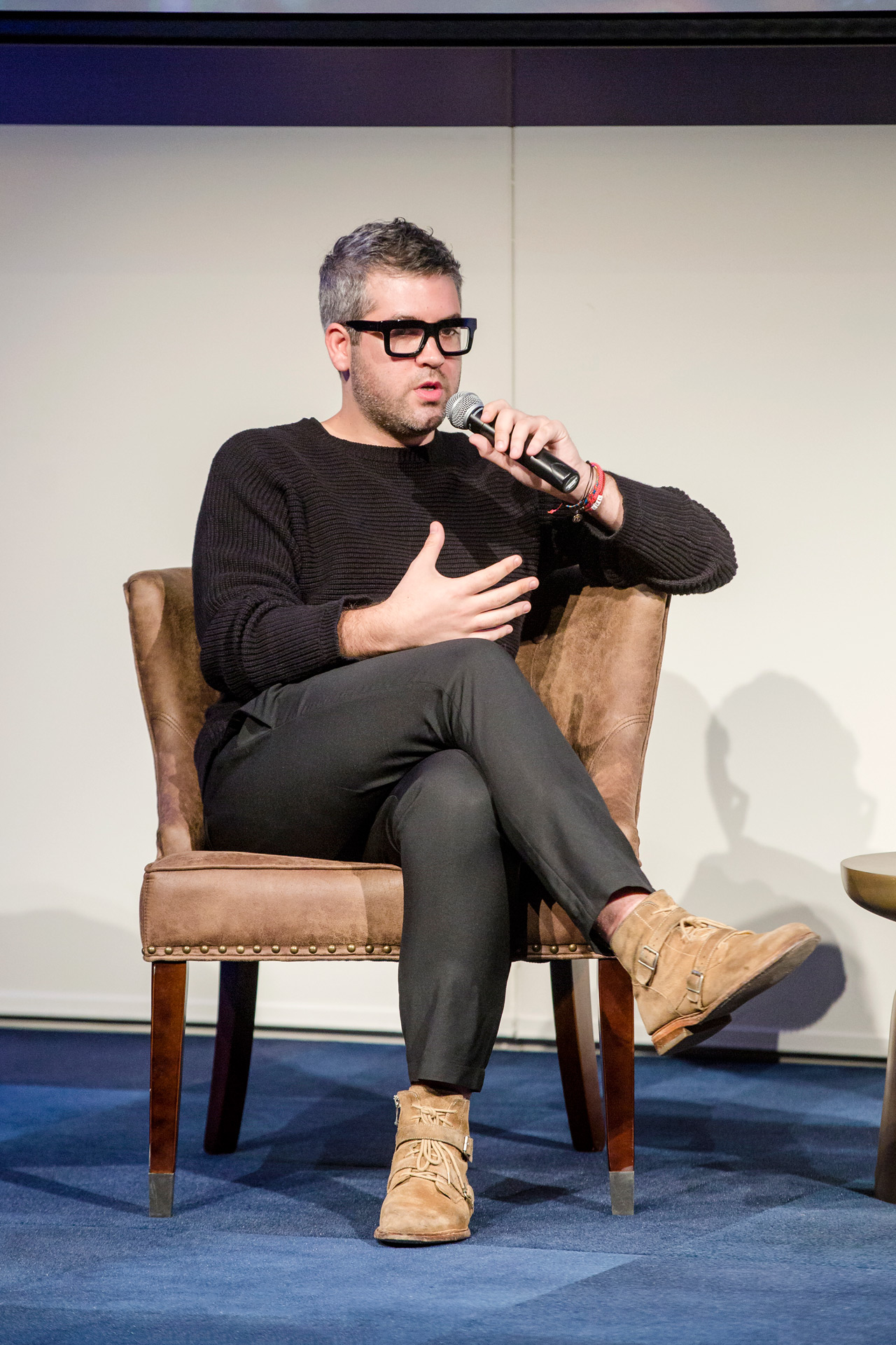 Brandon Maxwell sits with legs crossed on stage