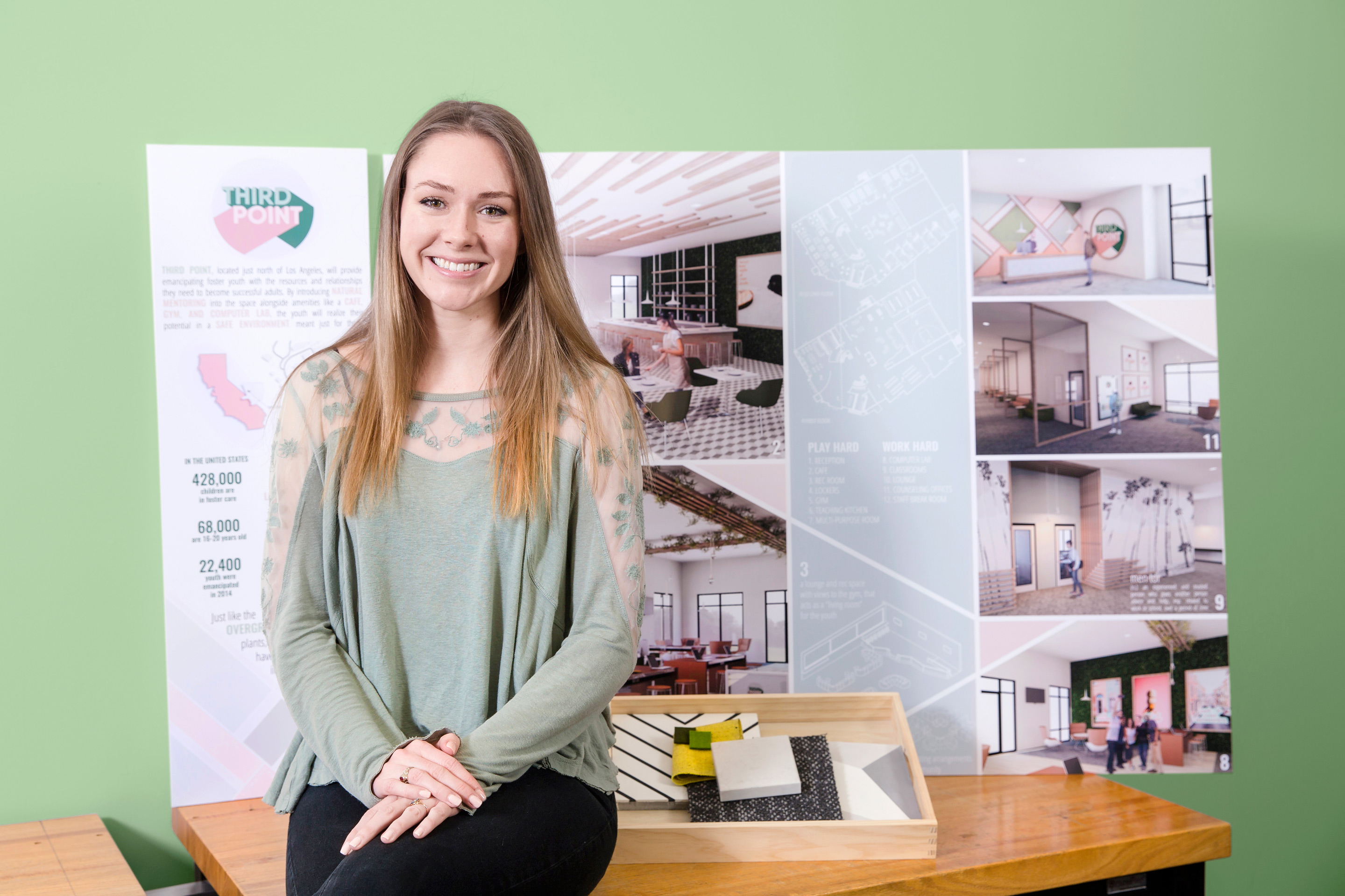 Interior design student sits in front of a poster of her work with material samples at her side