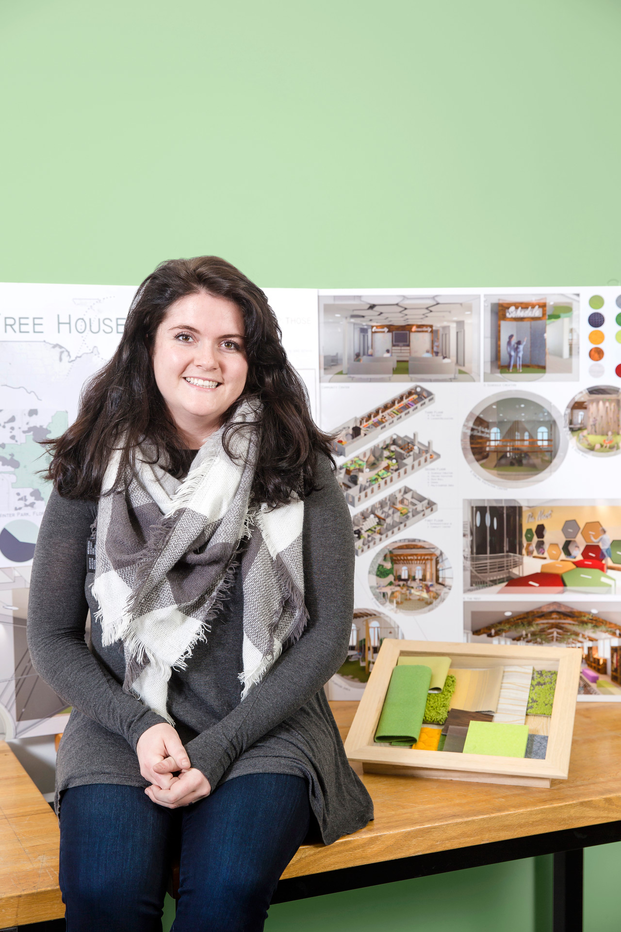 Interior design student sits in front of a poster of her work with lime green material samples at her side