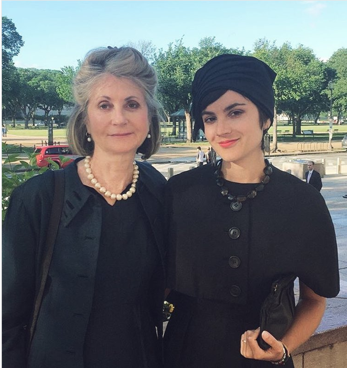 Two women wearing black one in pearls and the other wearing a hat