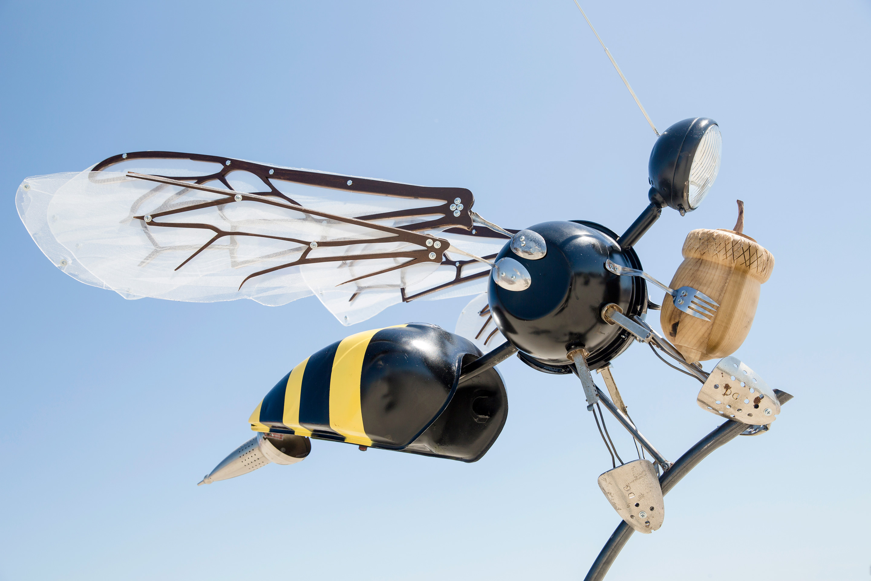 Large wind sculpture of a bee holding an acorn and made of recycled components 