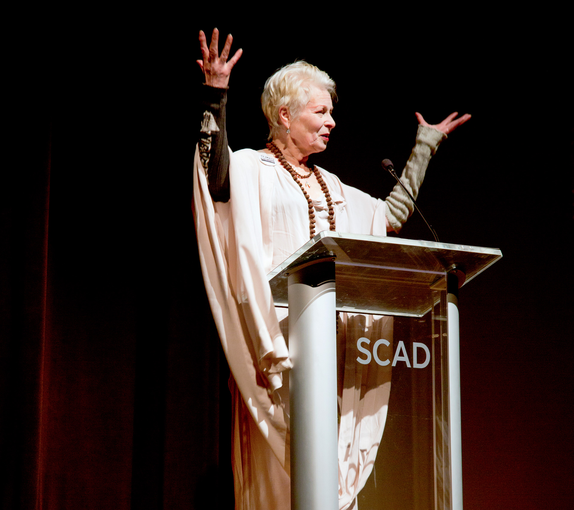 Vivienne Westwood raises her arms as she speaks at SCAD event