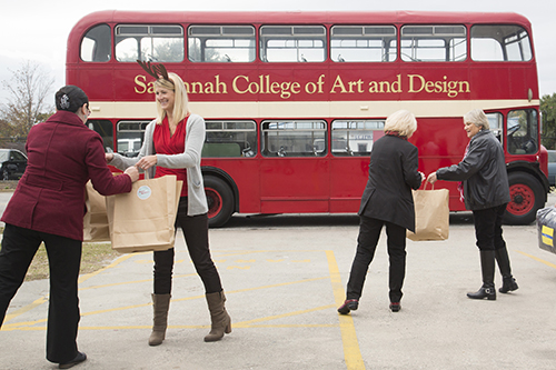 Students gather bags full of gifts in front of SCAD double-decker bus
