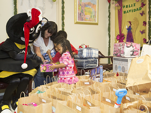Small children look closely at their gifts next to SCAD's mascot