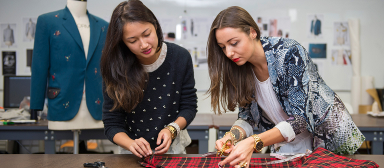 Fashion professor measuring and cutting fabric with student