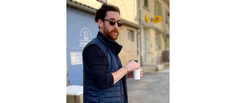 SCAD painting alum William Ruller stirs a cup of coffee while standing on French city street.