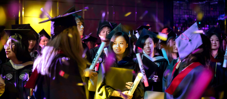 Group of students in cap and gowns hold diplomas