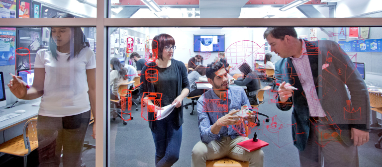 Students strategize together on a glass wall covered in hand-written notes