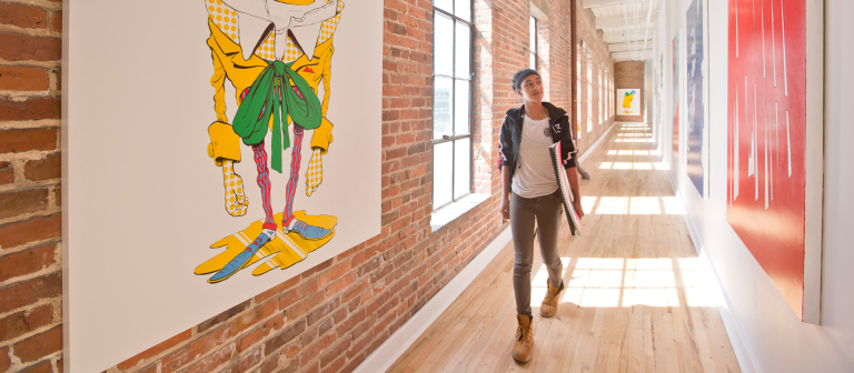 Alexander Hall, SCAD Savannah walks in long hallway while looking at hanging artwork