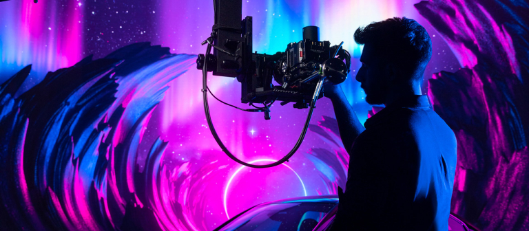Student films car on LED volume stage against purple and magenta background.