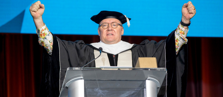 Commencement speaker John Lasseter at podium with outstretched arms