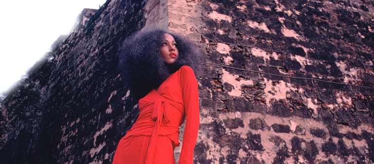 Pat Cleveland in red two-piece matte jersey skirt with wrap top and matching red stockings and shoes Pat Cleveland in red two-piece matte jersey skirt with wrap top and matching red stockings and shoes