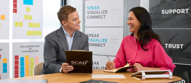 Man and woman sitting at a table having a discussion while holding a SCAD portfolio.