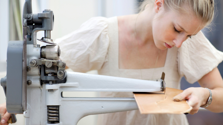 Accessory design student using machine to cut leather