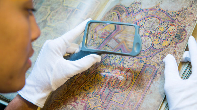 Art history student using magnifying glass to study book