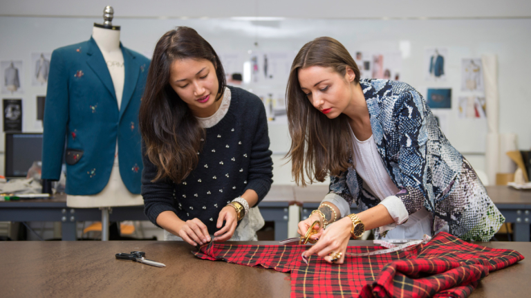 Fashion professor measuring and cutting fabric with student Fashion professor measuring and cutting fabric with student
