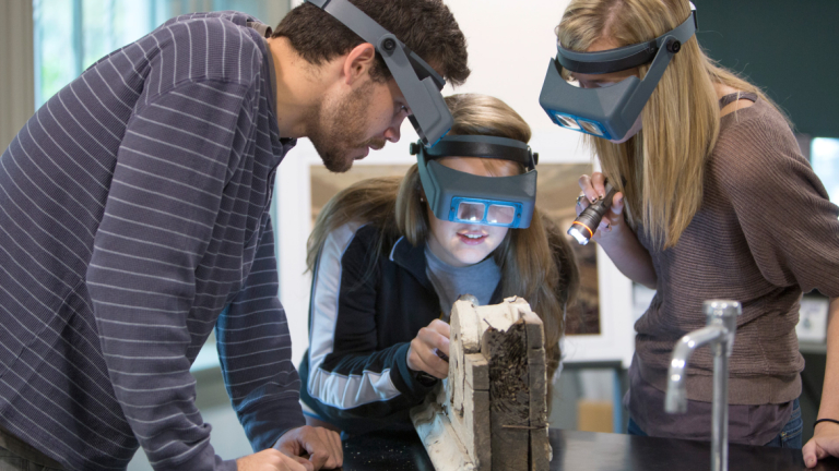 Preservation design students using magnifying glasses to examine object