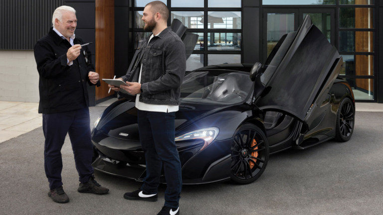 Mentor and student standing in front of black sports car.