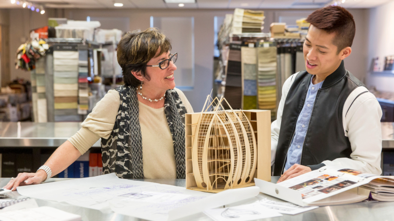 Interior design professor looking at building model with student