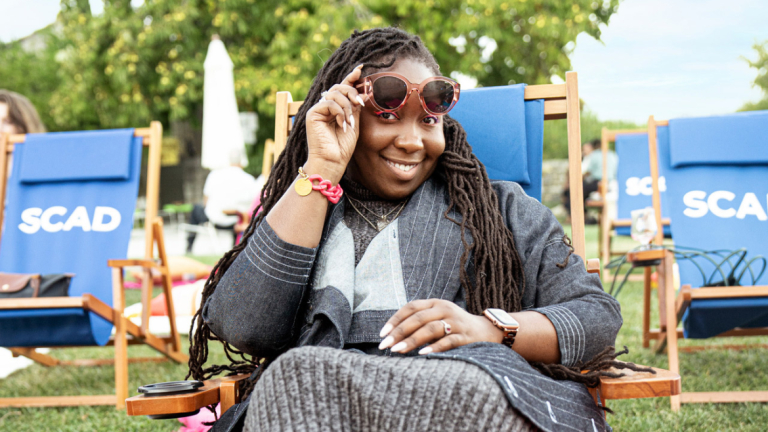 A woman smiling lifting her sunglasses