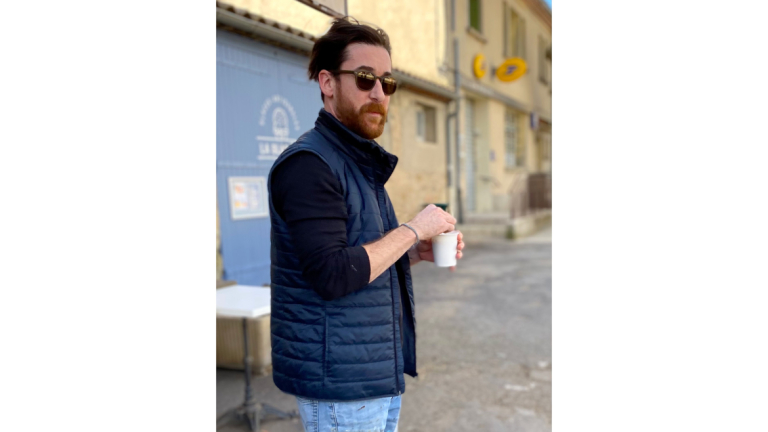 SCAD painting alum William Ruller stirs a cup of coffee while standing on French city street.