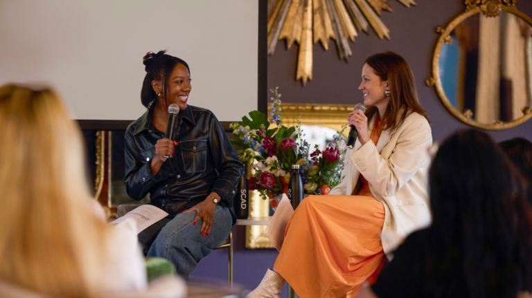 Two female speakers sitting and smiling at each other.