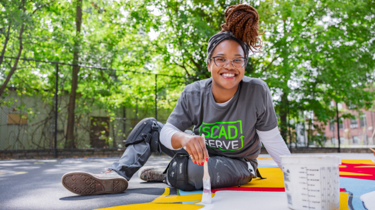 SCAD SERVE volunteer paints a basketball court