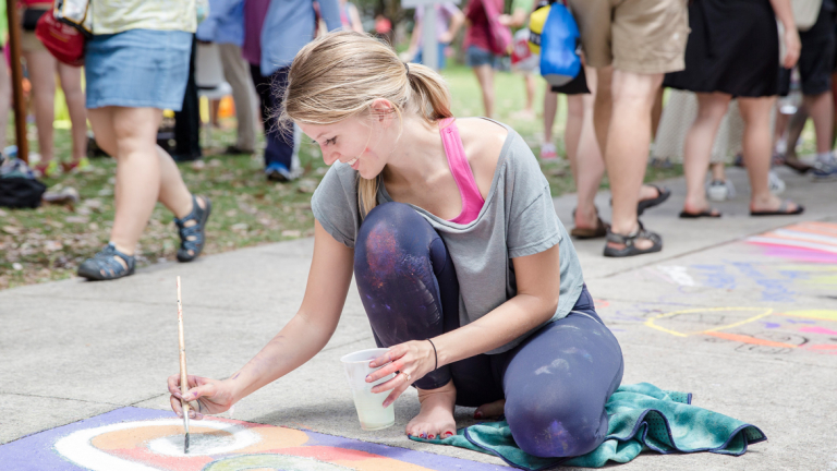 Young woman uses a paint brush to create her sidewalk chalk masterpiece