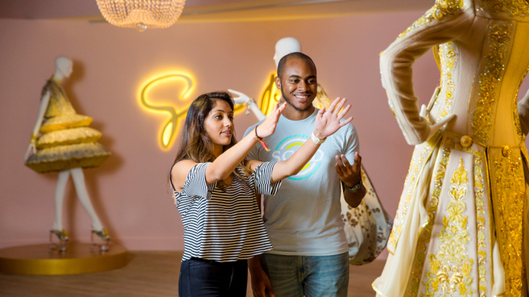 SCAD fashion students examine a gold and white garment on mannequin