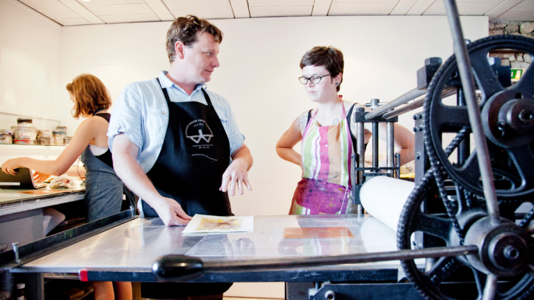 Printmaking professor instructing student at printing press Printmaking professor instructing student at printing press