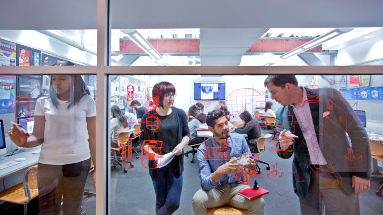 Students strategize together on a glass wall covered in hand-written notes