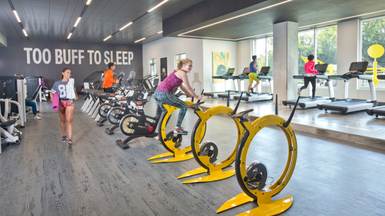 Student works out on brightly colored stationary yellow bike in modern gym setting