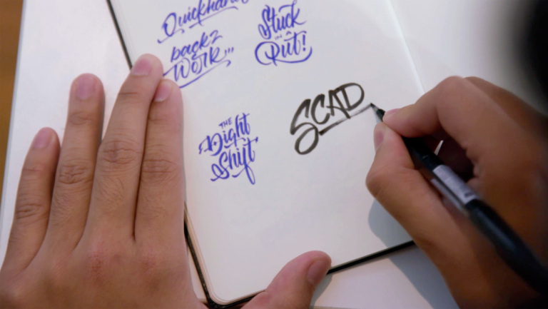 hand writing SCAD in a notebook