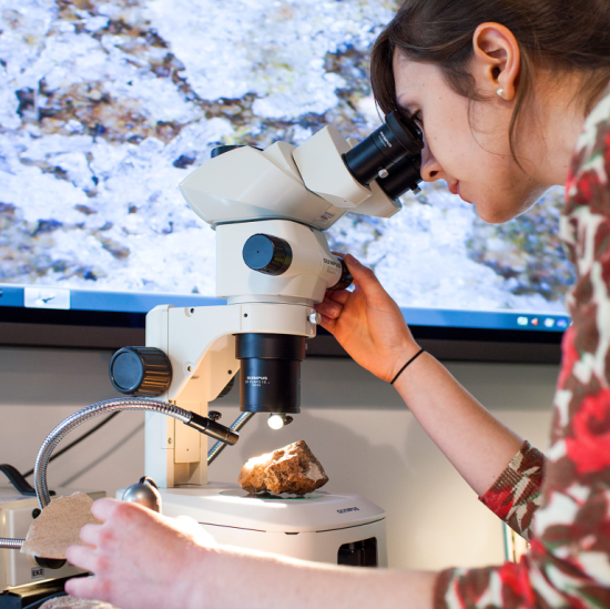 Preservation design student using microscope to examine artifact