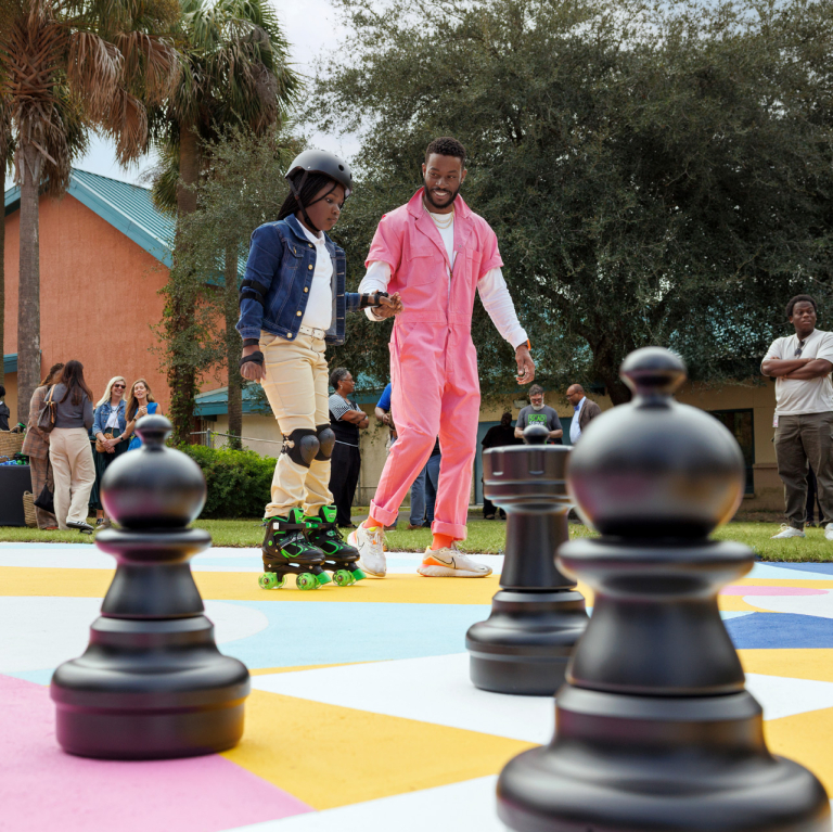 SCAD SERVE volunteer helps a student skate on a Paint Our Parks court